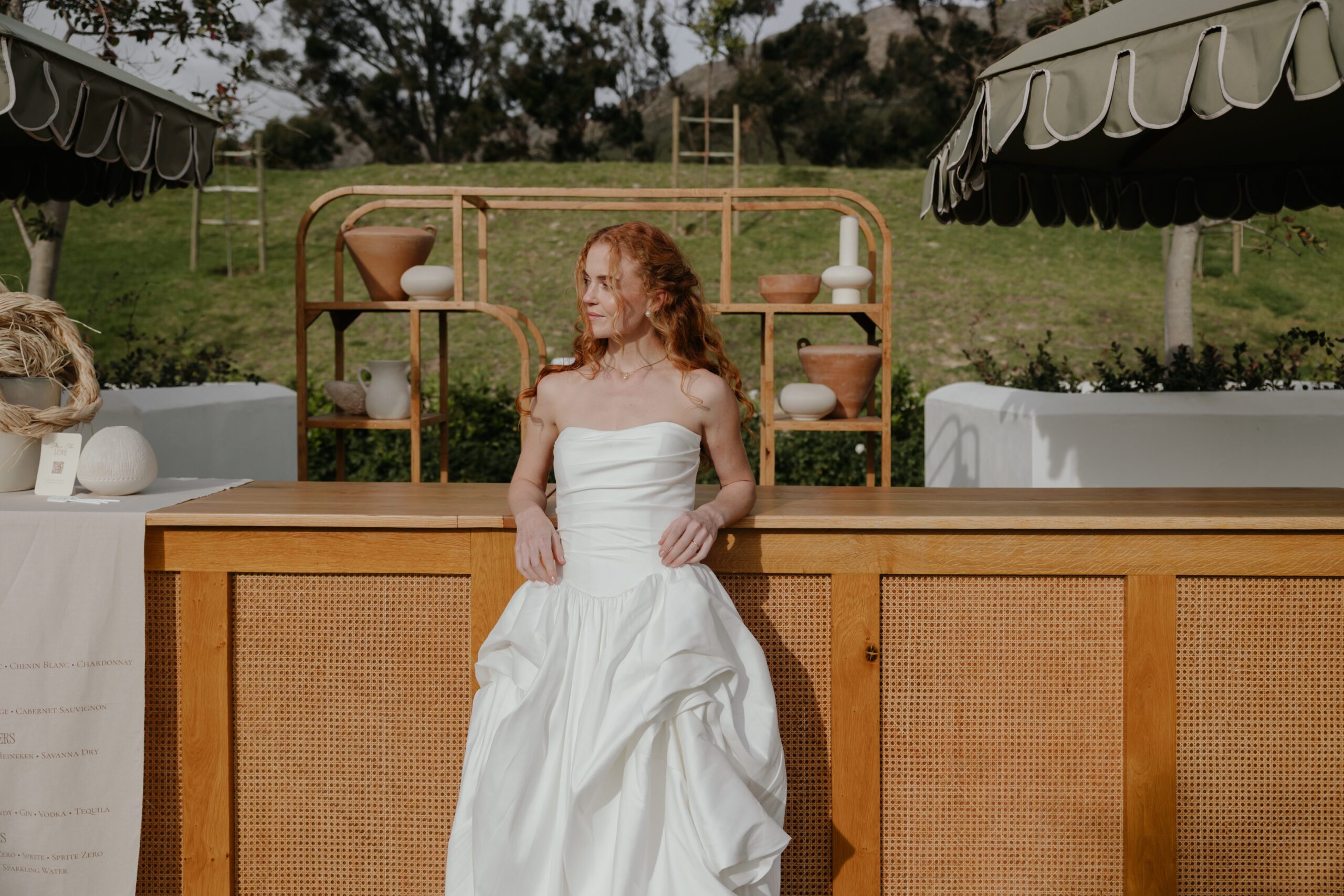 Bride posing at a stylish outdoor wooden bar with natural décor and event furniture by a|CREATE