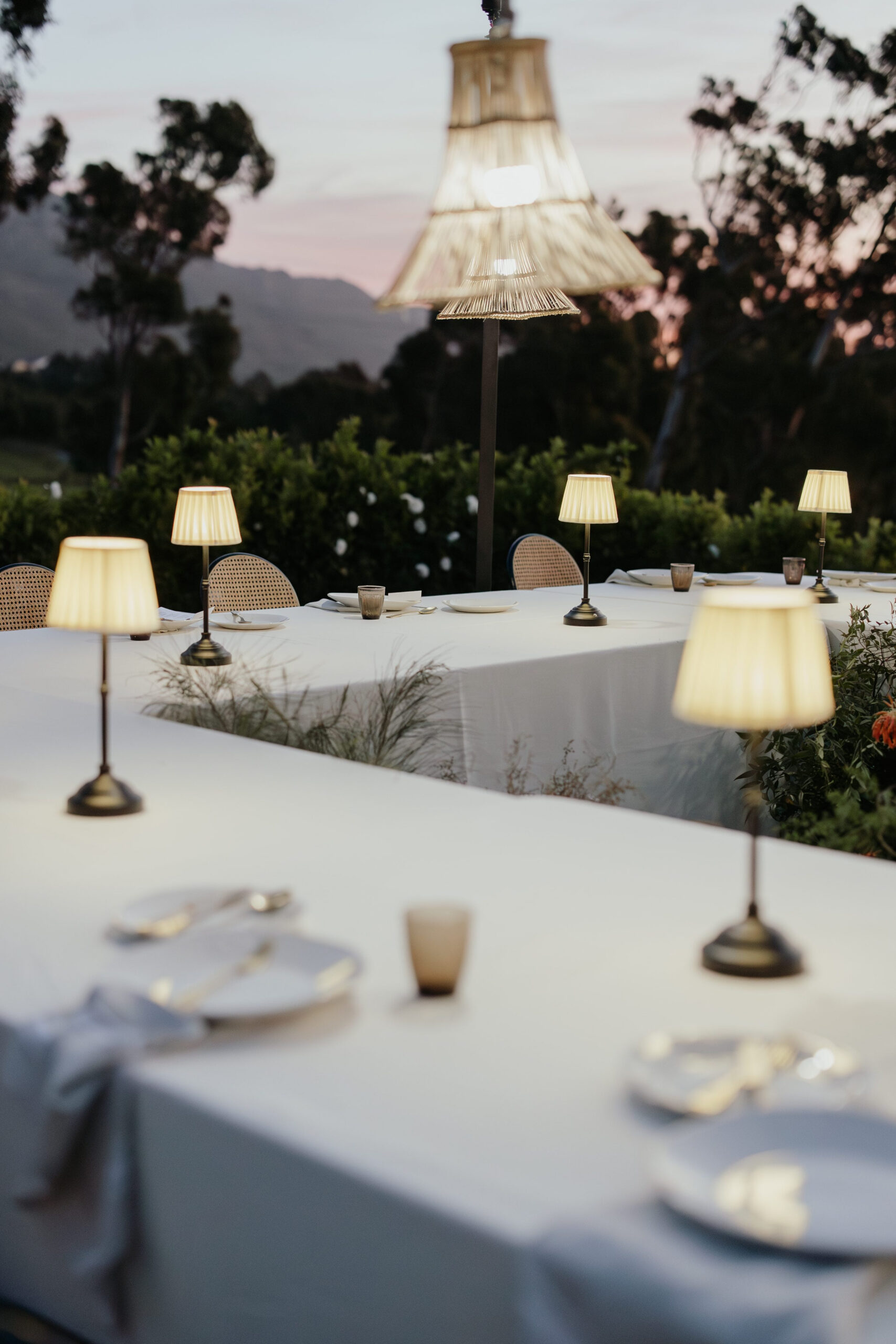 Outdoor wedding reception at sunset with elegant table lamps, woven pendant lighting and refined tablescape styling by a|CREATE