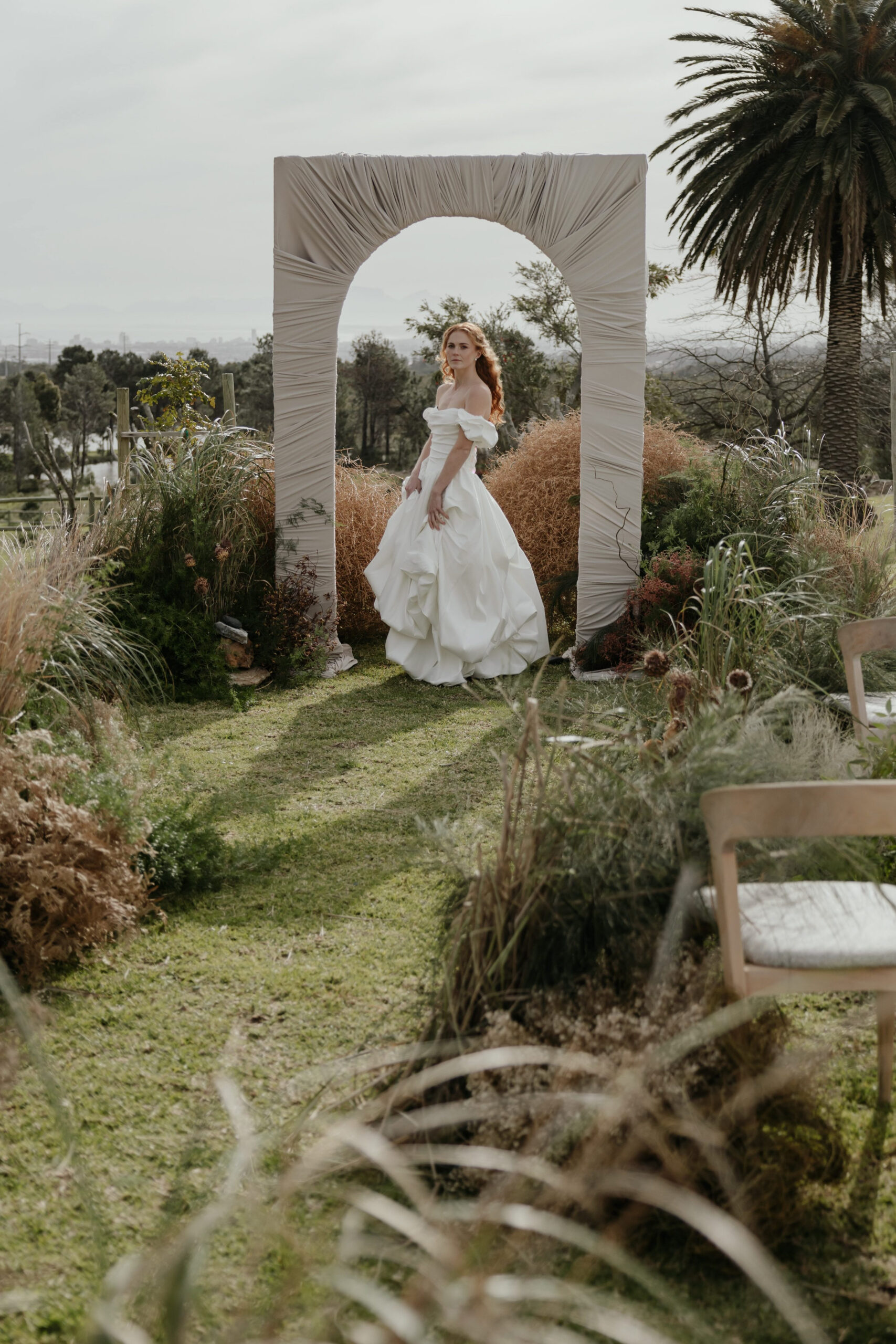 Acreate Styled Shoot Bride at an outdoor wedding ceremony with natural grass styling, wooden seating and a draped arch by a|CREATE